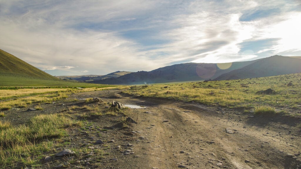 mongolian altai. dirt road and mountain valley in beams of the evening sun. smoking chimney of traditional yurt nomads. nature and travel. mongolia