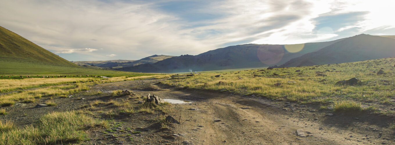 mongolian altai. dirt road and mountain valley in beams of the evening sun. smoking chimney of traditional yurt nomads. nature and travel. mongolia