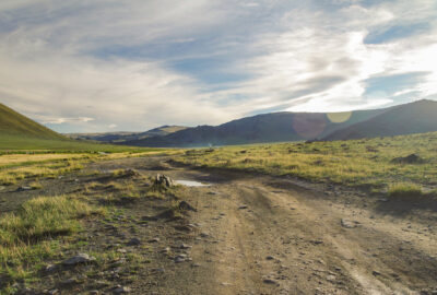 mongolian altai. dirt road and mountain valley in beams of the evening sun. smoking chimney of traditional yurt nomads. nature and travel. mongolia