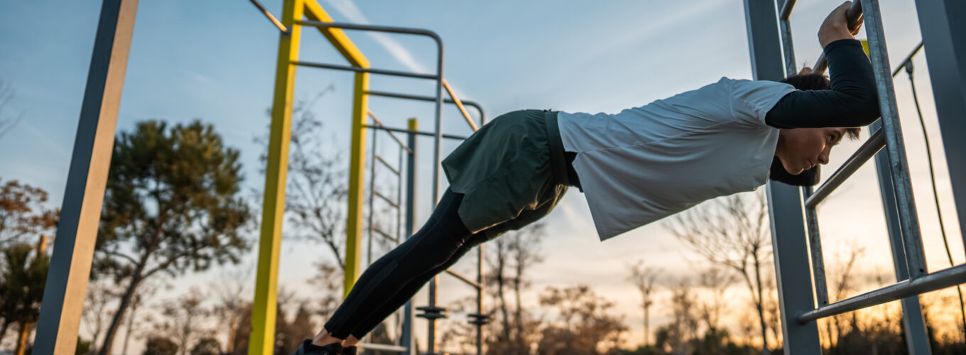 young athletic man exercising at fitness calisthenics workout and stretching legs and back at street gym during sunset, body improvement and strength training concept