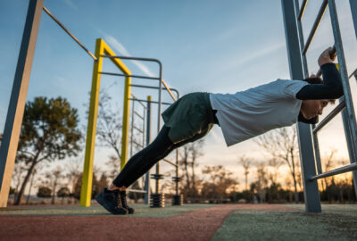 young athletic man exercising at fitness calisthenics workout and stretching legs and back at street gym during sunset, body improvement and strength training concept